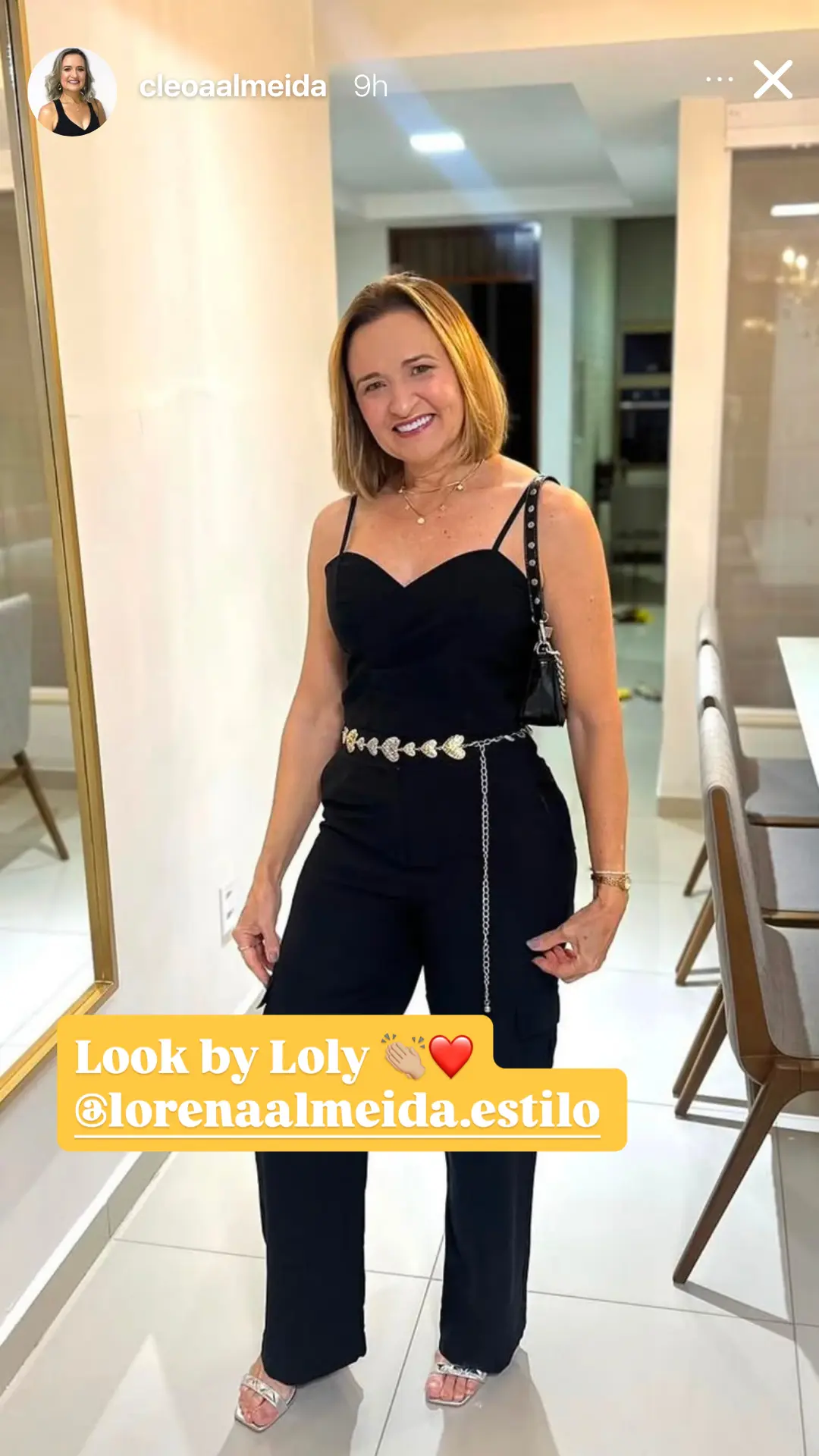 Story no Instagram de @cleoaalmeida usando macacão preto com cinto de correntes, legendado “Look by Loly”.